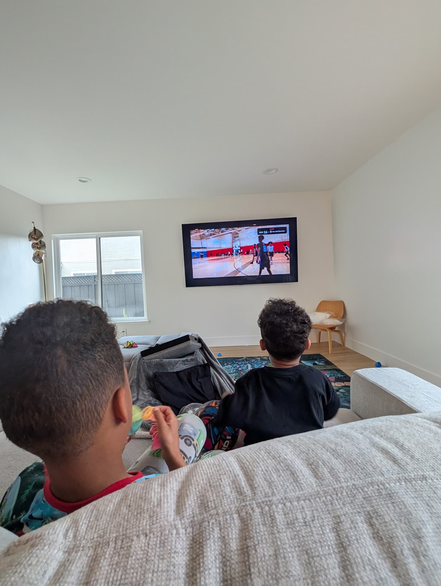 Two kids watching their sibling's basketball game live on the living room TV via the team app
